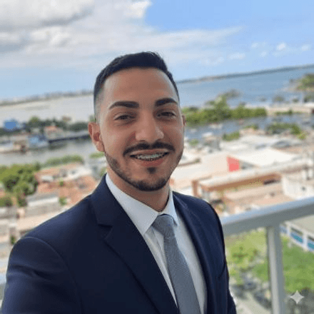 Rodrigo Brinate Protázio, desenvolvedor full-stack e analista de infraestrutura, sorrindo em traje formal com vista de cidade ao fundo